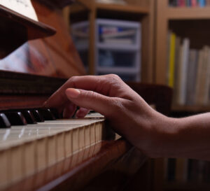 Caucasian girl playing piano at home. Selective focus. Blured white and black piano keys in foreground. Play musical scales with one hand.